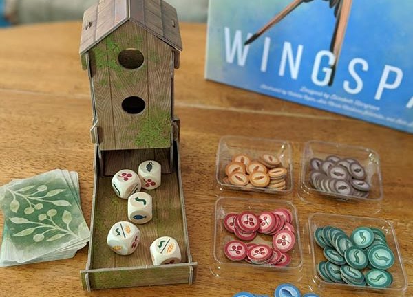 Overhead view of cardboard dice tower that looks like a bird feeder with custom wooden dice in the tray next to food tokens.