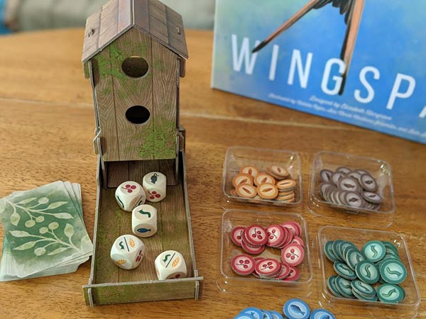 Overhead view of cardboard dice tower that looks like a bird feeder with custom wooden dice in the tray next to food tokens.